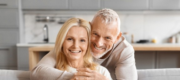 Älteres Pärchen umarmt sich lächelnd auf Couch