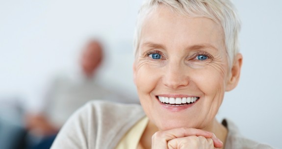 Ätere Frau lacht mit Gesicht auf Kinn gestützt