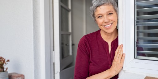 Ältere Frau lehnt lächelnd am Türrahmen