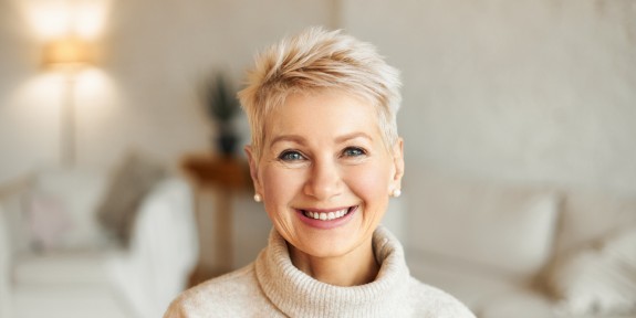 Ältere Frau in Wohnzimmer lächelt freundlich