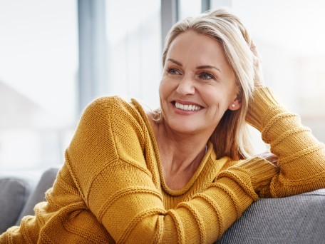 Frau stütz sich auf Sofalehne und Lacht